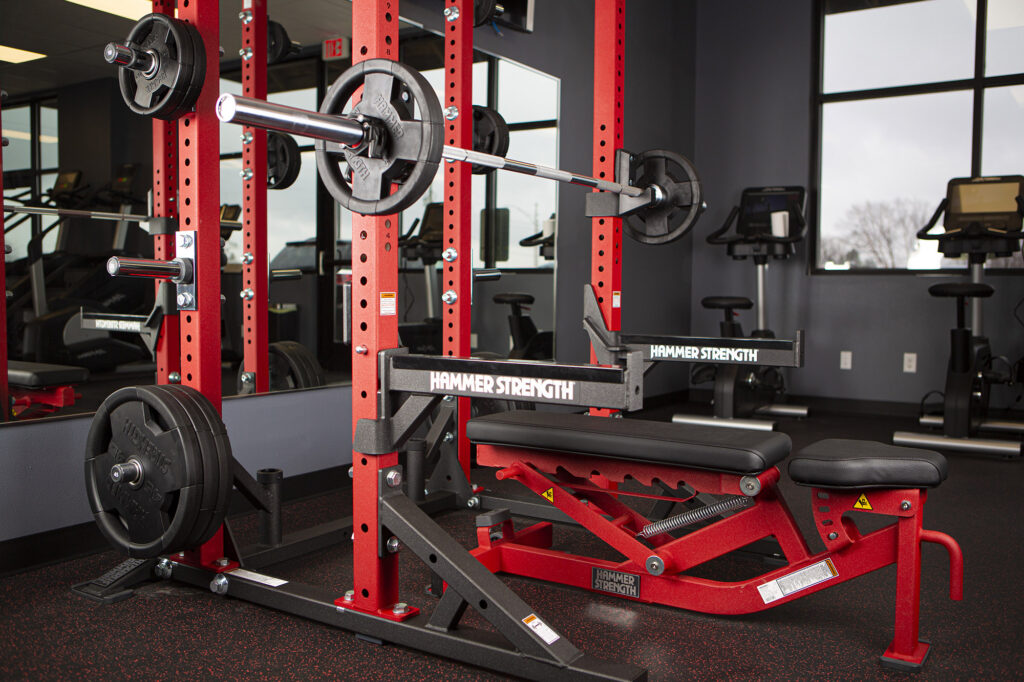A red and black weight bench with elliptical machines line up next to it