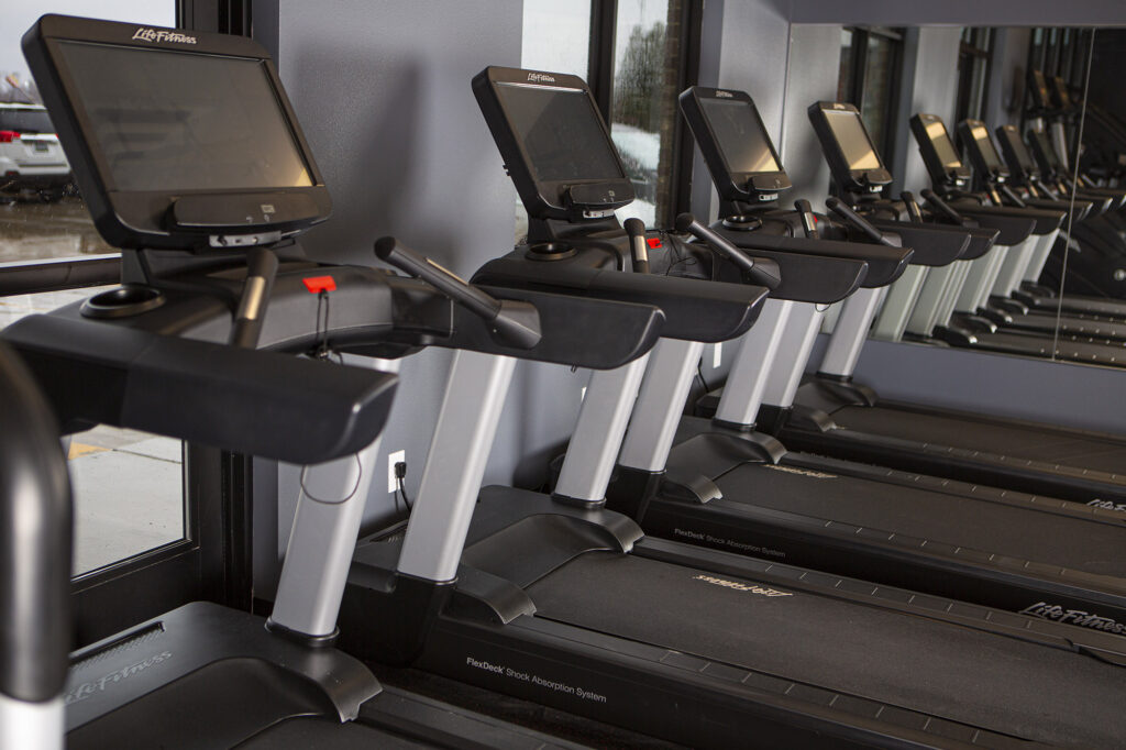 A row of black and silver treadmills with screens